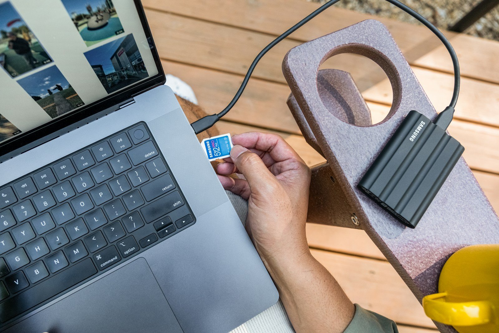 Hand inserting sd card into laptop next to external hard drive.